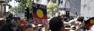 Indigenous rights protesters with sign "We are still here" held up.