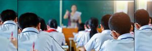 Image shot from behind of rows of students listening to a teacher at the front of the classroom.