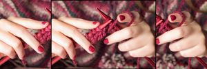 A close up of a woman's hands with red fingernails knitting a red jumper.