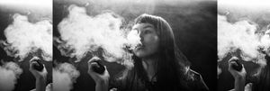 Black and white image of girl exhaling smoke from a vape.